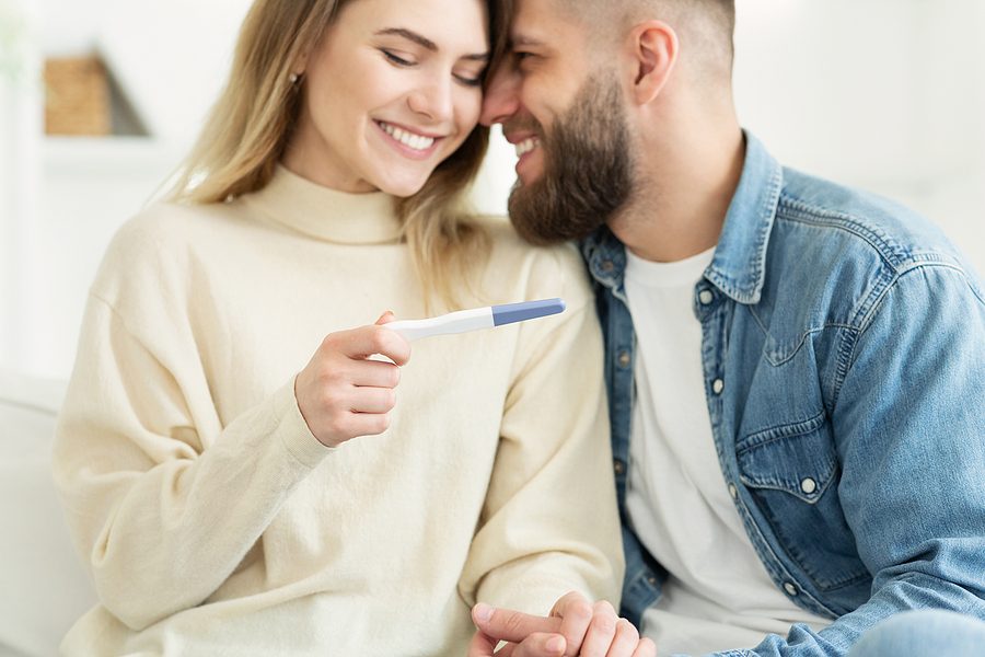 Happy couple checking pregnancy test with positive result, man embracing woman