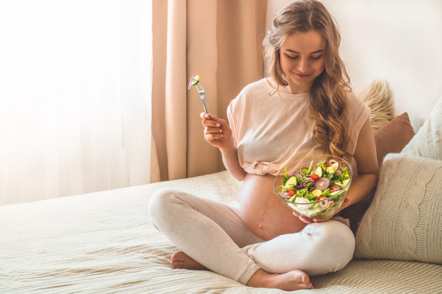 Pregnancy and healthy organic nutrition. Pregnant woman enjoying fresh vegetable salad in bed, free space. Concept of expectation and health.